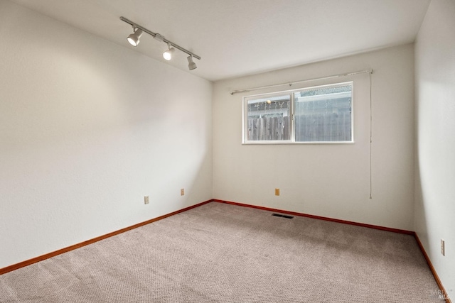 carpeted empty room featuring visible vents, rail lighting, and baseboards