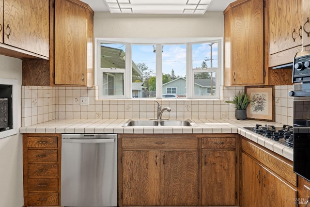 kitchen with a sink, tile counters, brown cabinetry, and stainless steel dishwasher