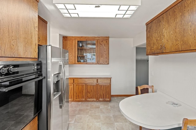 kitchen with baseboards, brown cabinetry, glass insert cabinets, oven, and stainless steel refrigerator with ice dispenser