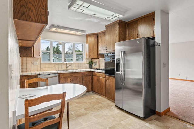 kitchen with brown cabinetry, decorative backsplash, stainless steel appliances, and a sink