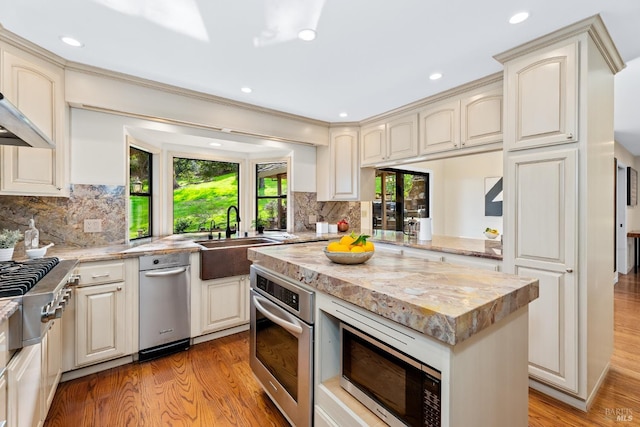 kitchen with appliances with stainless steel finishes, a sink, light wood finished floors, and light stone countertops