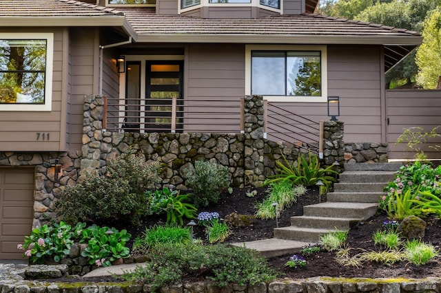 view of side of home featuring a garage, stone siding, and a tile roof