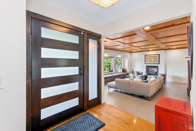 entrance foyer featuring a glass covered fireplace, coffered ceiling, baseboards, and light tile patterned floors