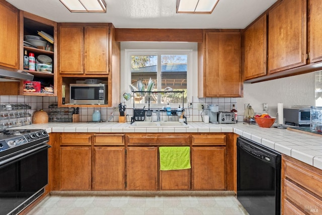 kitchen with decorative backsplash, tile countertops, brown cabinets, black appliances, and a sink