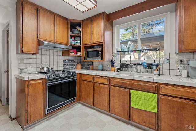 kitchen featuring tile countertops, under cabinet range hood, light floors, stainless steel microwave, and gas range