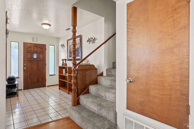 foyer with visible vents, stairway, a textured ceiling, and light tile patterned floors