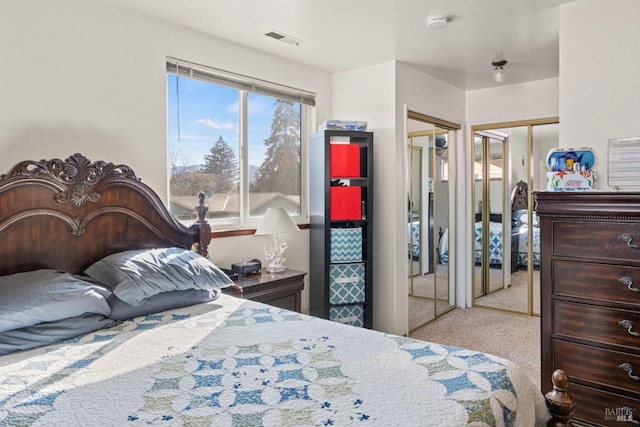 bedroom with multiple closets, light colored carpet, and visible vents