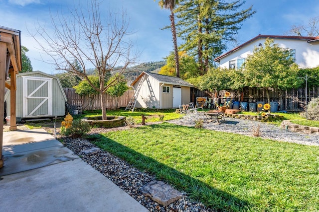 view of yard with a fire pit, a fenced backyard, an outbuilding, a storage unit, and a patio area