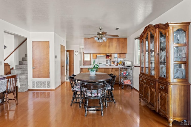 dining room featuring stairway, light wood-type flooring, visible vents, and a ceiling fan