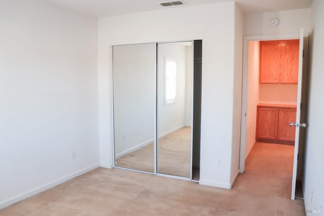 unfurnished bedroom featuring baseboards, a closet, light carpet, and visible vents