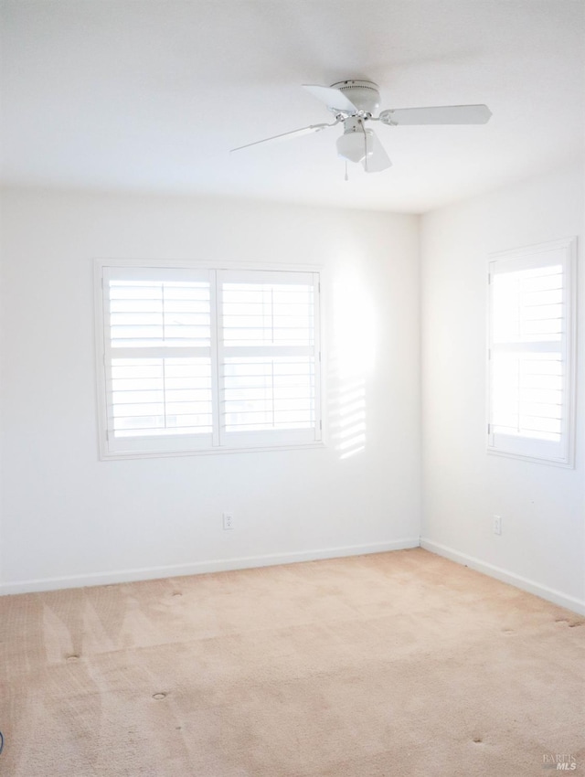 spare room featuring light colored carpet, baseboards, and ceiling fan