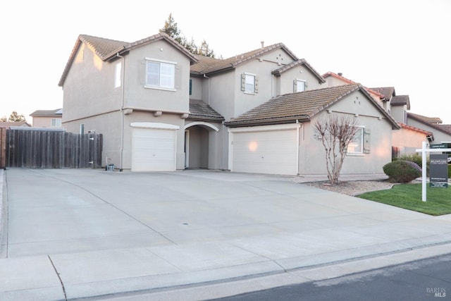 view of front of home with stucco siding, a tiled roof, concrete driveway, and fence