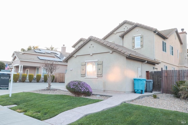 view of front of house featuring stucco siding, a front lawn, a tile roof, fence, and a chimney