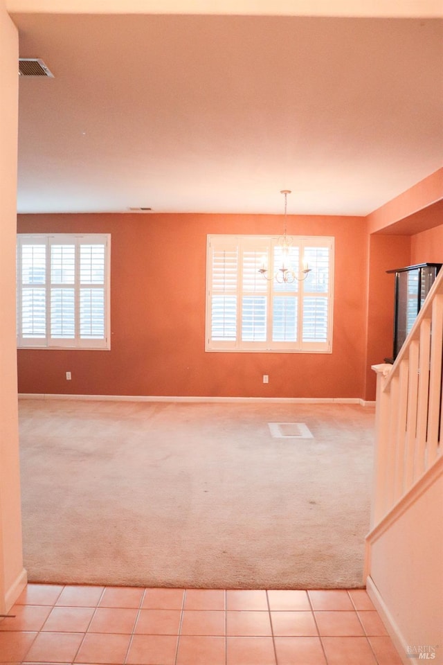 empty room with a wealth of natural light, light colored carpet, a chandelier, and stairs