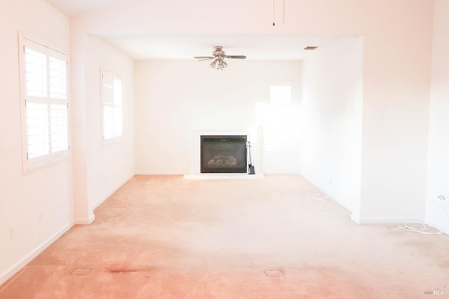 unfurnished living room featuring visible vents, baseboards, ceiling fan, light carpet, and a glass covered fireplace