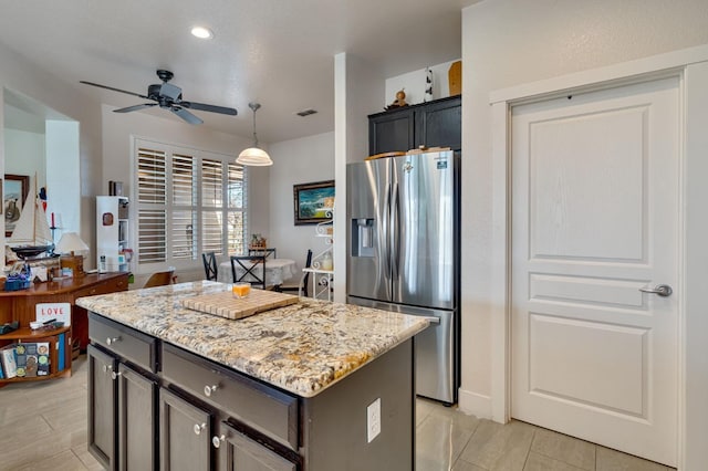 kitchen with visible vents, a center island, ceiling fan, light stone countertops, and stainless steel refrigerator with ice dispenser