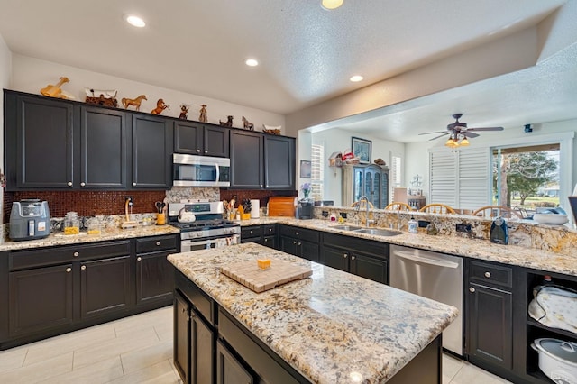 kitchen featuring tasteful backsplash, light stone countertops, recessed lighting, appliances with stainless steel finishes, and a sink