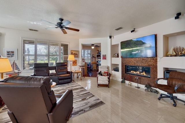 living area with a tiled fireplace, a textured ceiling, visible vents, and ceiling fan