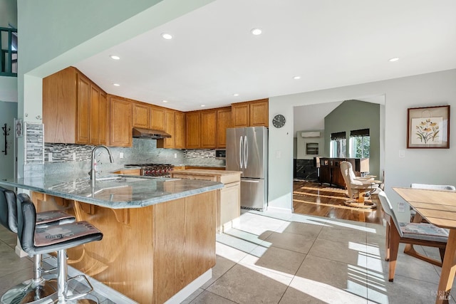 kitchen featuring appliances with stainless steel finishes, a sink, under cabinet range hood, and decorative backsplash