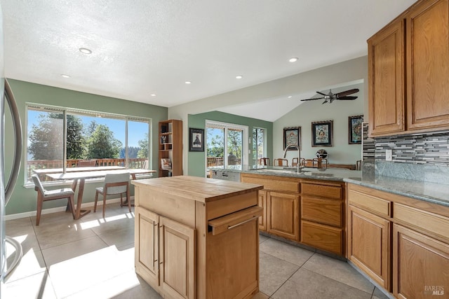 kitchen with light tile patterned floors, a peninsula, vaulted ceiling, wooden counters, and backsplash