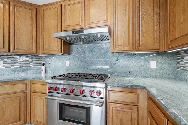 kitchen featuring tasteful backsplash, brown cabinetry, light stone countertops, high end stainless steel range oven, and under cabinet range hood