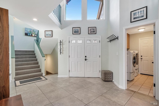 entrance foyer featuring light tile patterned floors, baseboards, washer and clothes dryer, a towering ceiling, and stairway