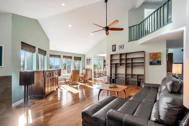 living area featuring a ceiling fan, high vaulted ceiling, light wood-style flooring, and baseboards