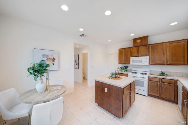 kitchen with white appliances, visible vents, brown cabinetry, a kitchen island, and light countertops