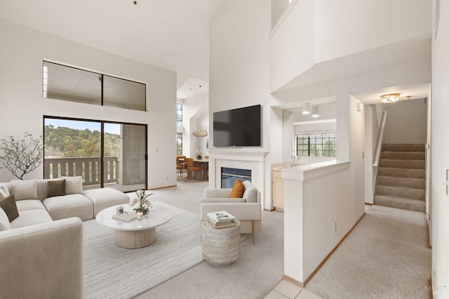 living area with light carpet, baseboards, a glass covered fireplace, stairs, and a high ceiling