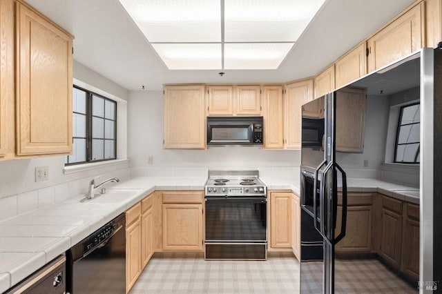 kitchen with light floors, light brown cabinets, a sink, and black appliances