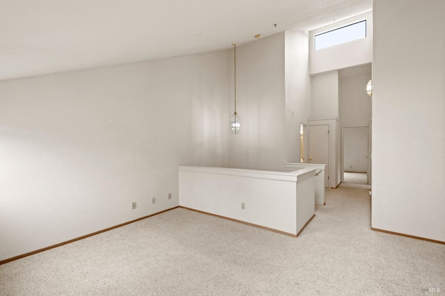 unfurnished room with a towering ceiling, baseboards, and light colored carpet
