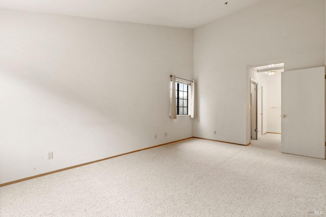 empty room featuring light carpet, a towering ceiling, and baseboards