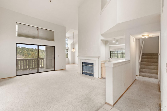 unfurnished living room with light carpet, a high ceiling, a premium fireplace, baseboards, and stairway