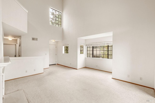 unfurnished living room featuring carpet floors, a towering ceiling, visible vents, and baseboards