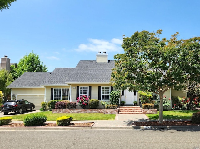 view of front of house featuring driveway, a shingled roof, a chimney, an attached garage, and a front lawn