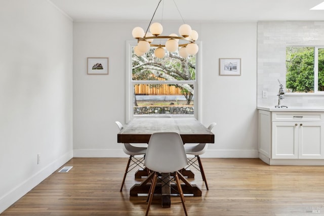 dining room with light wood-style floors, baseboards, visible vents, and an inviting chandelier