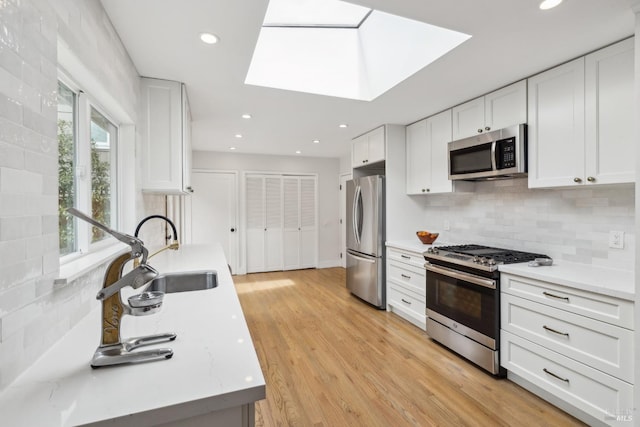 kitchen with light stone counters, decorative backsplash, appliances with stainless steel finishes, white cabinetry, and a sink