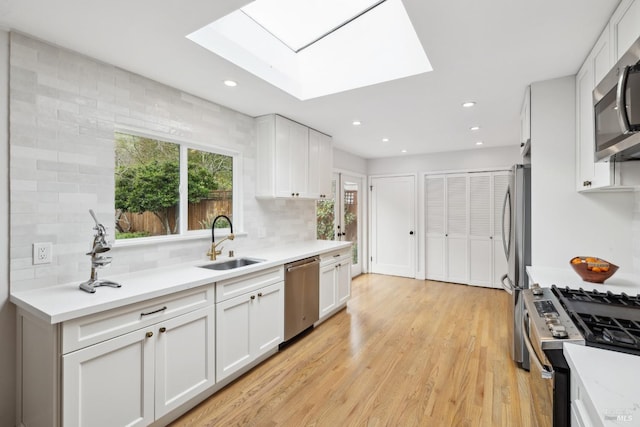 kitchen with a skylight, light countertops, appliances with stainless steel finishes, white cabinetry, and a sink