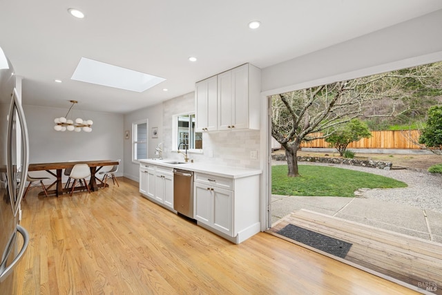 kitchen featuring tasteful backsplash, stainless steel appliances, light countertops, light wood-style floors, and white cabinetry