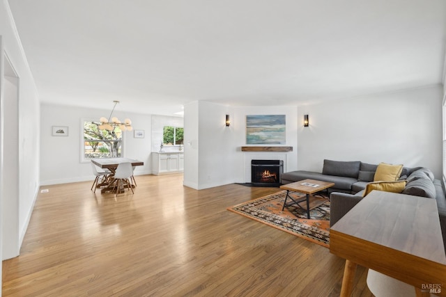 living area with light wood-style floors, baseboards, a fireplace with flush hearth, and an inviting chandelier