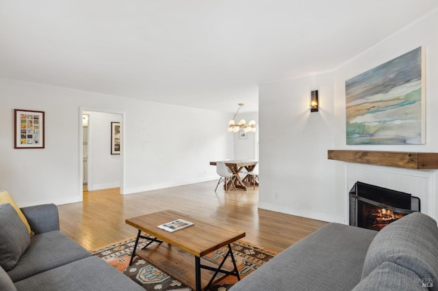 living room featuring an inviting chandelier, a lit fireplace, baseboards, and wood finished floors