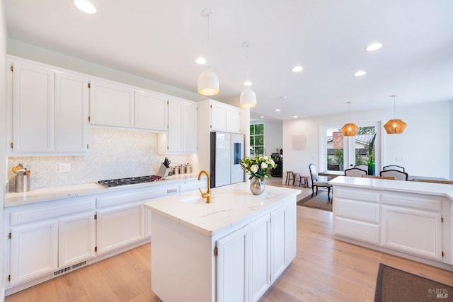 kitchen with stainless steel gas stovetop, white cabinets, a center island with sink, and freestanding refrigerator