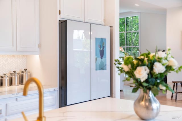 kitchen featuring light stone counters, decorative backsplash, white cabinetry, and freestanding refrigerator