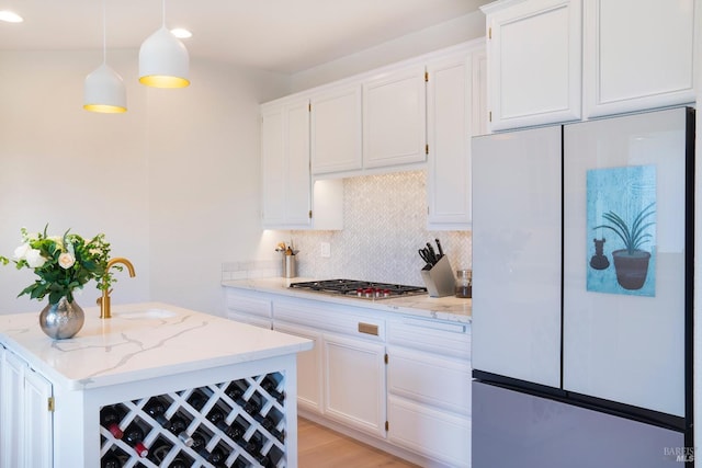 kitchen featuring decorative backsplash, freestanding refrigerator, stainless steel gas stovetop, white cabinets, and a sink