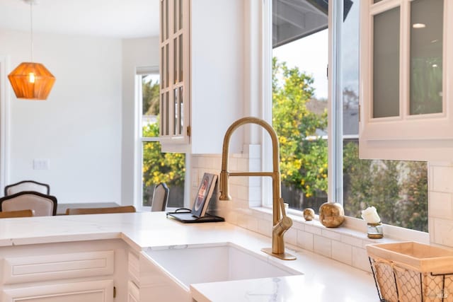 kitchen featuring a sink, tasteful backsplash, white cabinets, light stone countertops, and hanging light fixtures