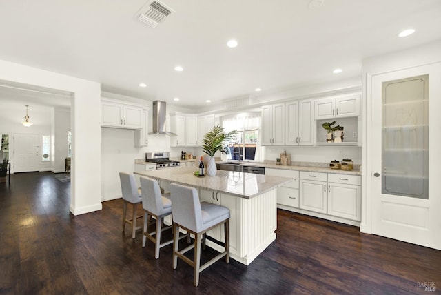 kitchen featuring wall chimney exhaust hood, visible vents, white cabinets, and a center island