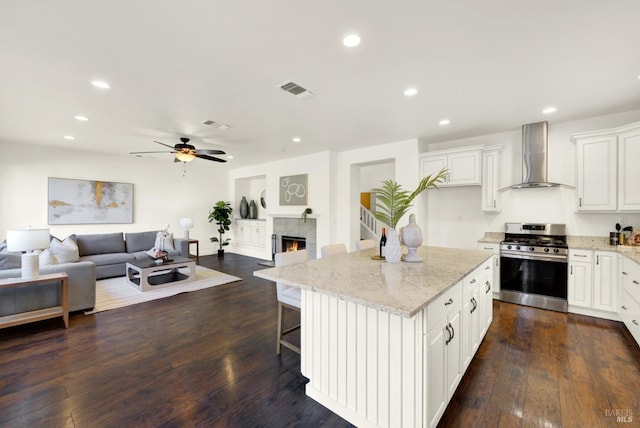 kitchen with open floor plan, stainless steel gas stove, wall chimney exhaust hood, and white cabinetry