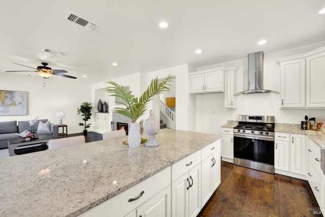 kitchen featuring stainless steel gas range oven, visible vents, white cabinetry, wall chimney range hood, and light stone countertops