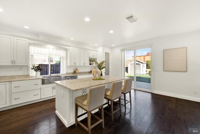 kitchen with a breakfast bar area, dark wood-type flooring, a kitchen island, white cabinets, and light stone countertops