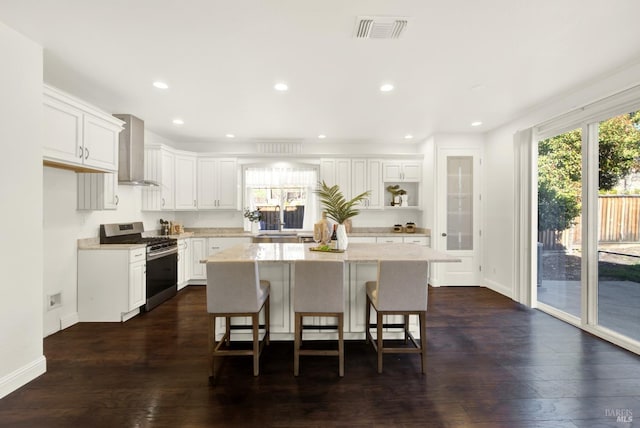 kitchen with a center island, visible vents, white cabinetry, gas range, and wall chimney exhaust hood